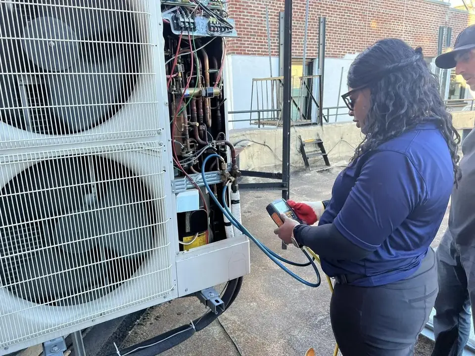 A Tauris Tech student taking meter readings on a condensing unit while the class watches